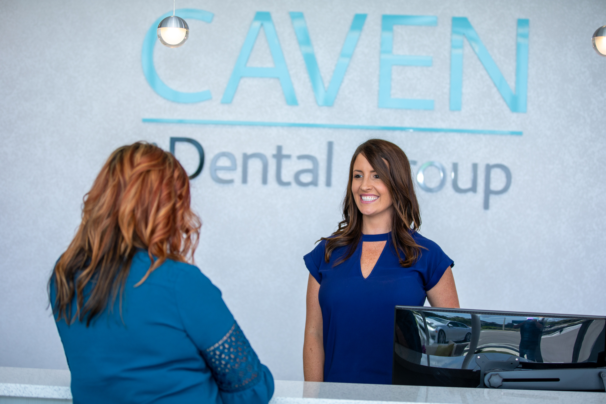 a patient setting up a porcelain veneers appointment with Dr. Caven's front desk lady in front of the practice logo.