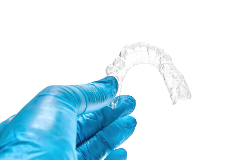 gloved dentist hand holding invisalign clear aligners.